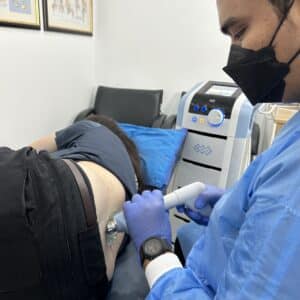Physiotherapist using shockwave therapy for a female patient during back pain treatment in KL